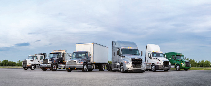 A scenic view of a lineup of Freightliner trucks against a backdrop of lush greenery.
